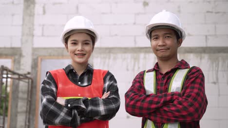 portrait of happy two asian construction workers wearing safety hard hats standing arms crossed in a construction site.