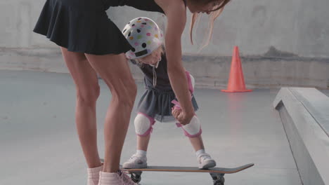 young woman teaching little daughter skateboarding