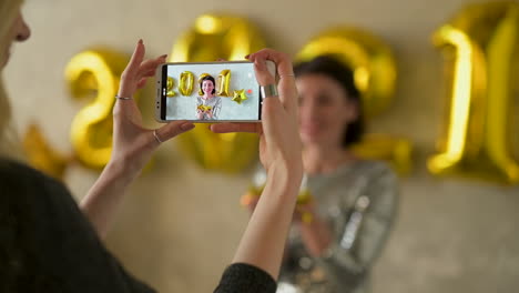 close up of hands taking a photo of a young pretty woman blowing gold glitter confetti and wearing evening dress