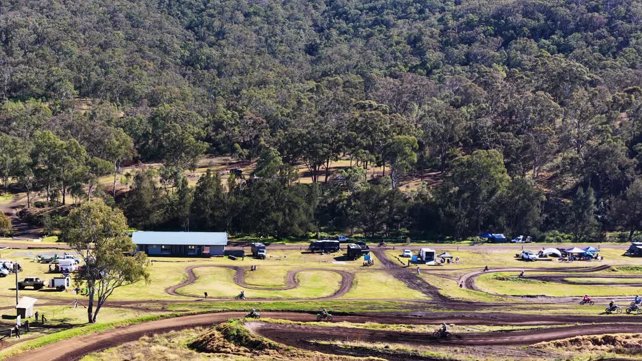 Multiple dirt bikes race on winding motocross track, sunny daylight, wide landscape, distant perspective