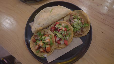 Plate-of-three-Mexican-meat-tacos,-sit-on-wood-table-top,-spinning-shot