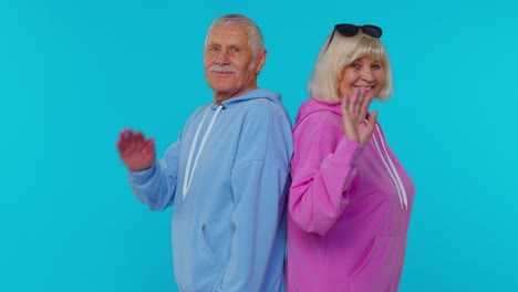 Elderly-granny-with-grandfather-turning,-smiling-at-camera-waving-hands-gesturing-hello-or-goodbye