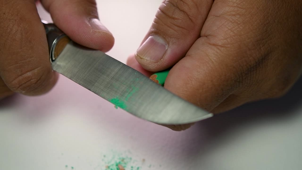 Footage of hands slowly sharpening a pencil and some coloured pencils with a sharp knife