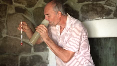 older caucasian vintner tasting fresh grape juice from test jar after measuring sweetness
