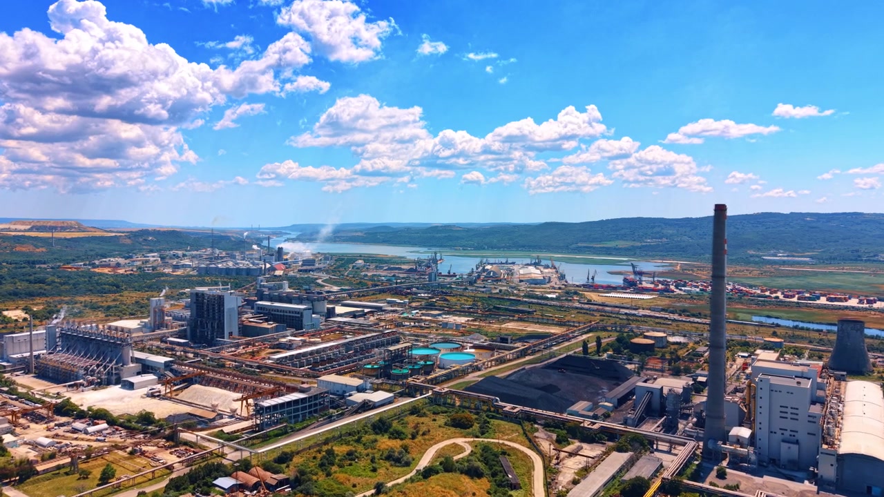 Vista aerea panoramica di un complesso di centrale elettrica. Grandi edifici industriali e alte ciminiere si ergono vicino a uno specchio d'acqua sotto un cielo luminoso