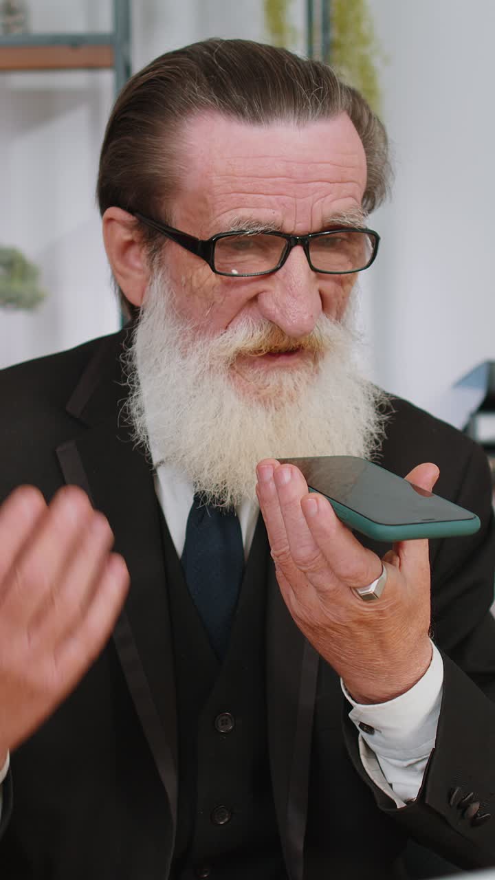 Uomo d'affari senior al lavoro, mentre parla al telefono cellulare in ufficio, utilizzando app di messaggistica.