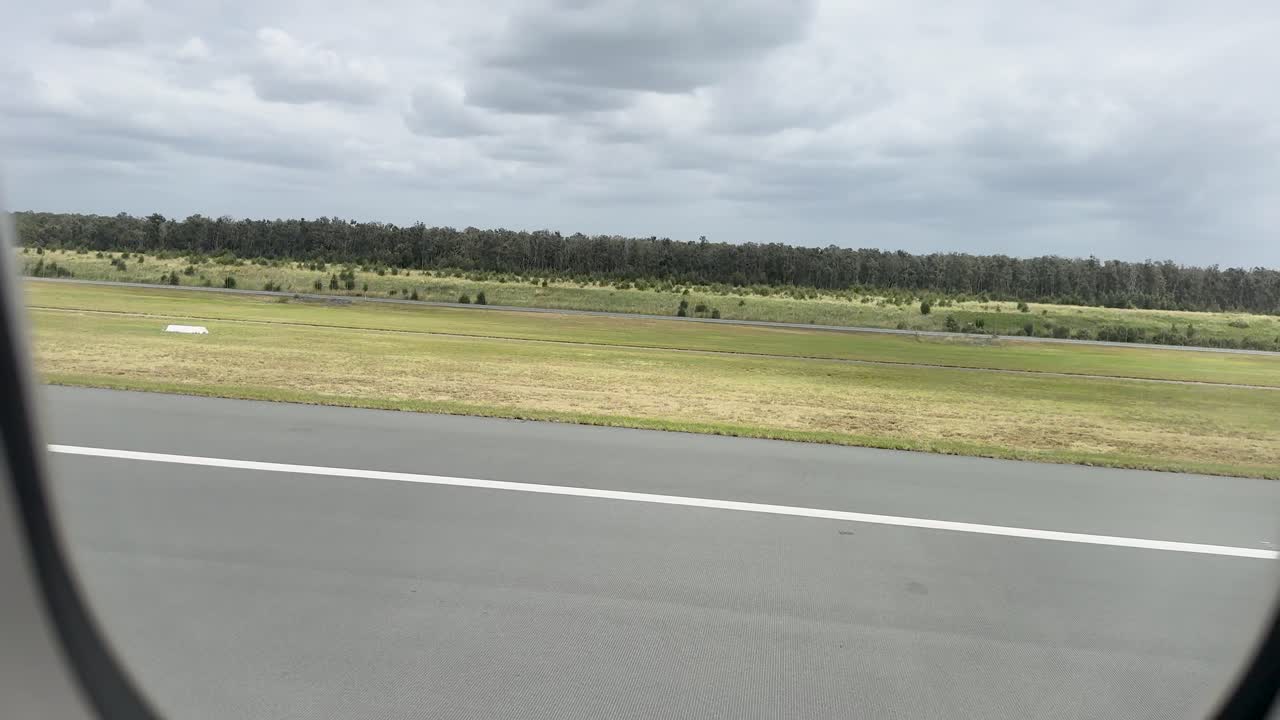 Aircraft moves along runway, exterior landscape visible through window, natural daylight, steady camera perspective