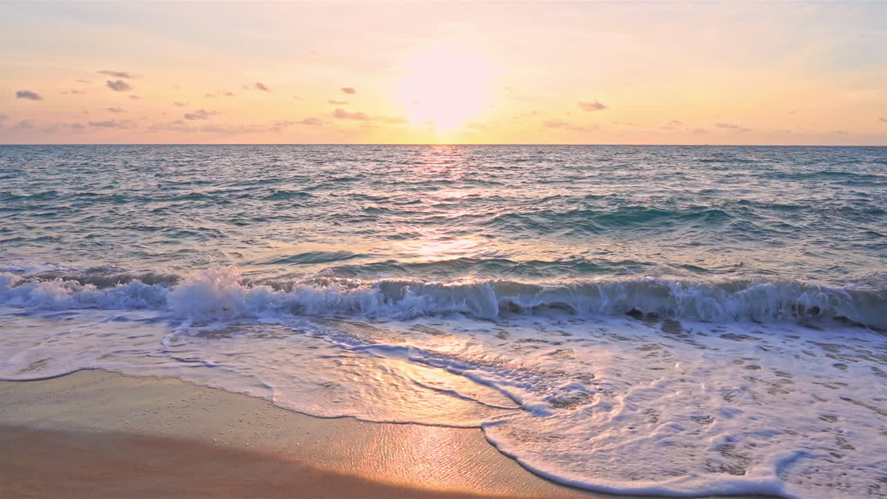 Slow-motion of the surf coming onshore while reflecting the pink, purple, orange, and yellow colors of a tropical sunset