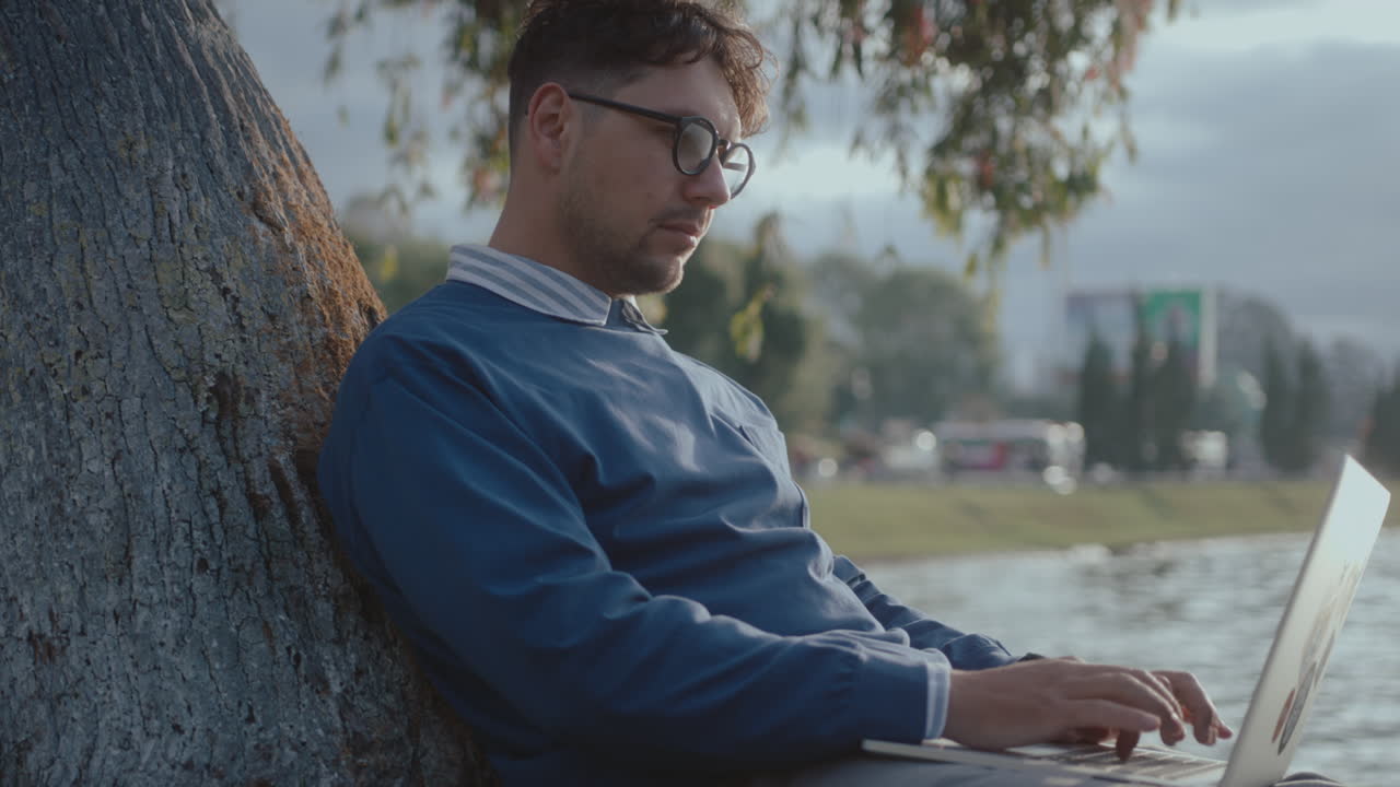 Man Sitting by Tree in the Park Typing on Laptop