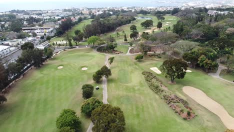 Vista-Aérea-Del-Campo-De-Golf-Jugadores-Profesionales-Practicando-El-Deporte,-Ciudad-De-Fondo