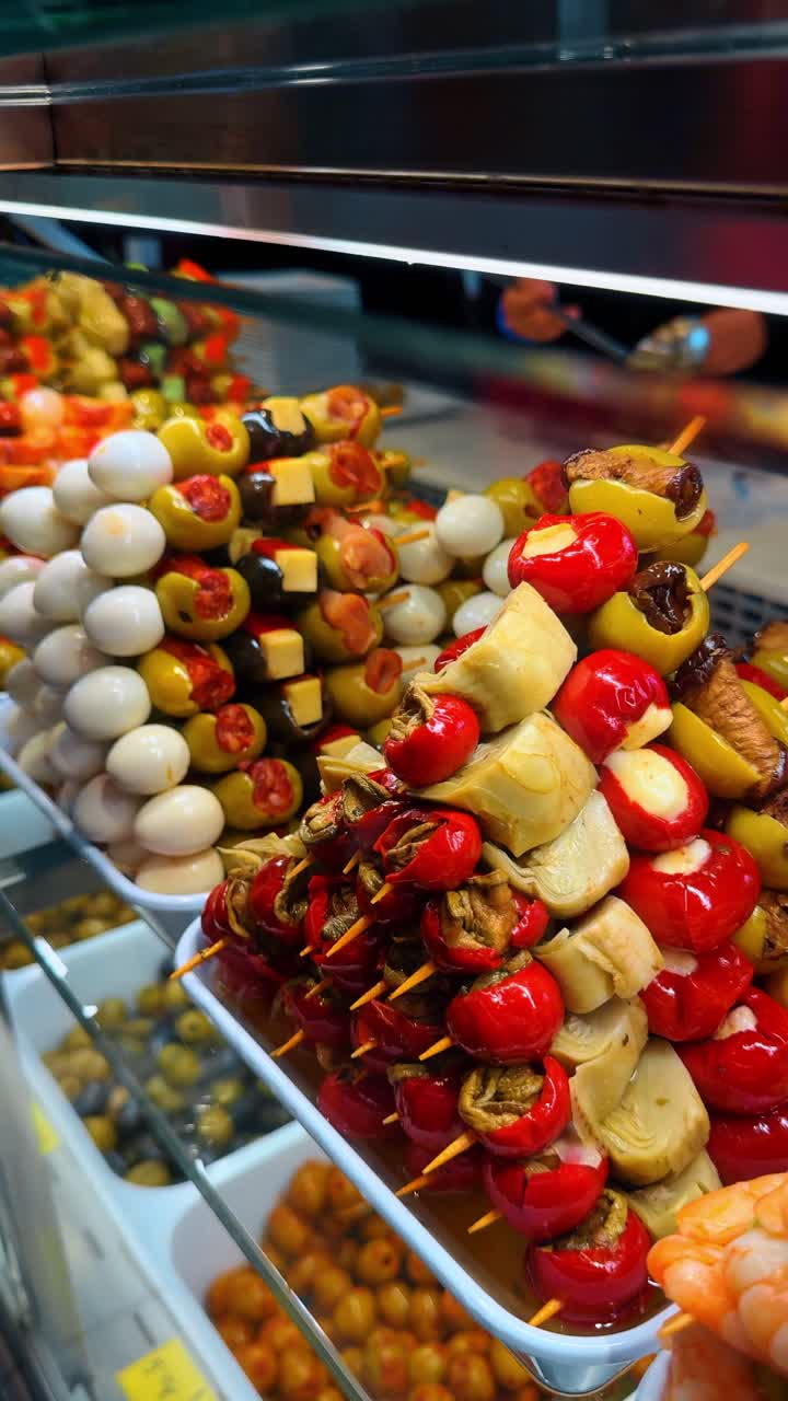 Madrid, Spagna, 2 agosto 2025: Spiedini di tapas spagnole assortite con olive e peperoni. Primo piano di vari spiedini di pintxos con olive verdi, peperoni rossi, carciofi e gamberi in un mercato.