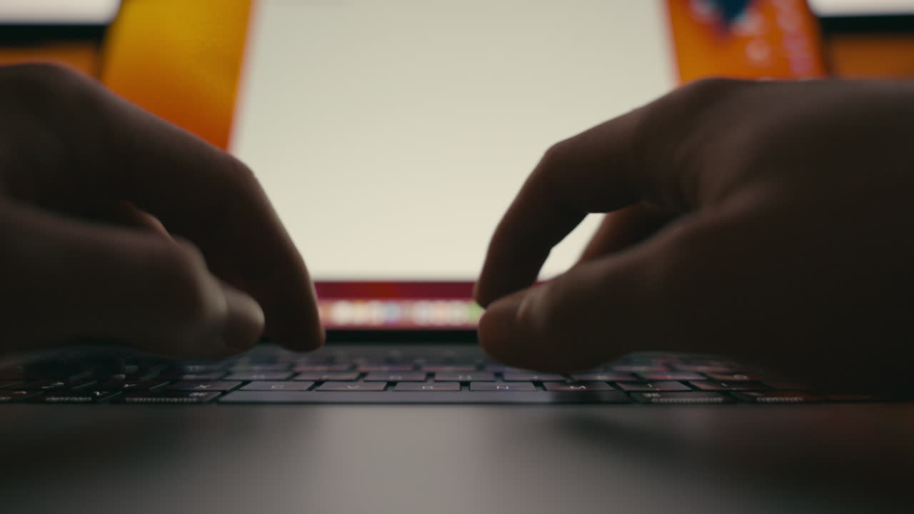 Closeup of hands typing on a laptop keyboard at night