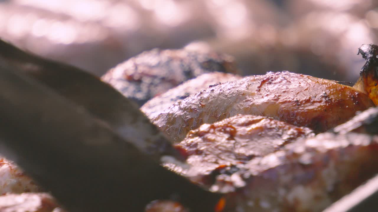 Chef Tongs Moving Chicken Drumsticks on BBQ with Smouldering Smoke Rising from Hot Charcoals Below. Lean Poultry High Protein Meat with Crispy Skin. Delicious Outdoor Barbecue Social Food.