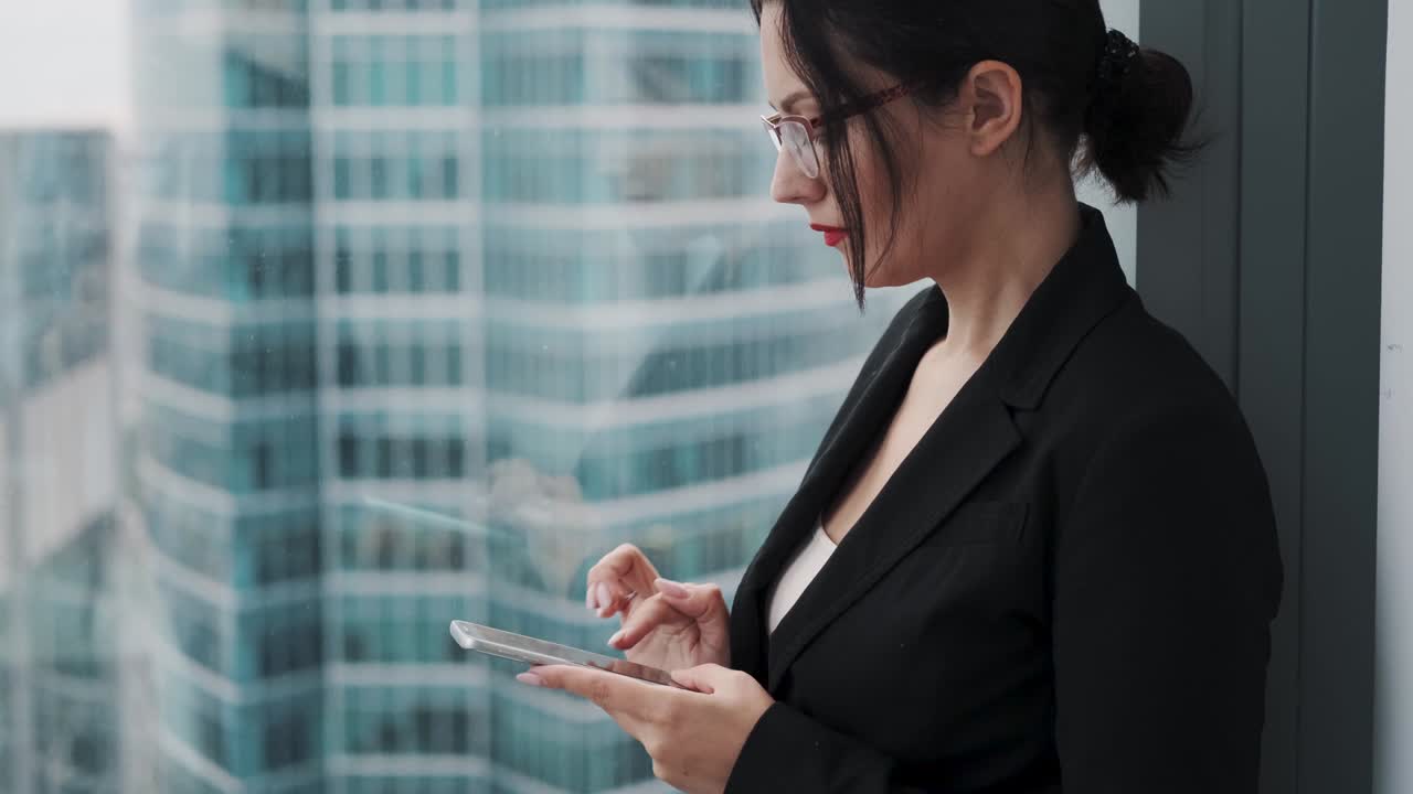 창문 근처의 마천루의 높은 층에 서서 드폰을 사용하는 사업가.