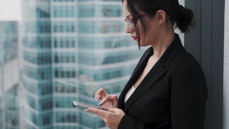 businesswoman using a cell phone while standing on a high floor of a skyscraper near a window.