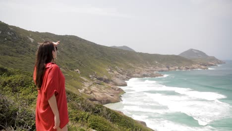 woman trying to spot something in the sea, looking closely, when she realizes being filmed, smiles and comes back to appreciate all the beauty of the landscape