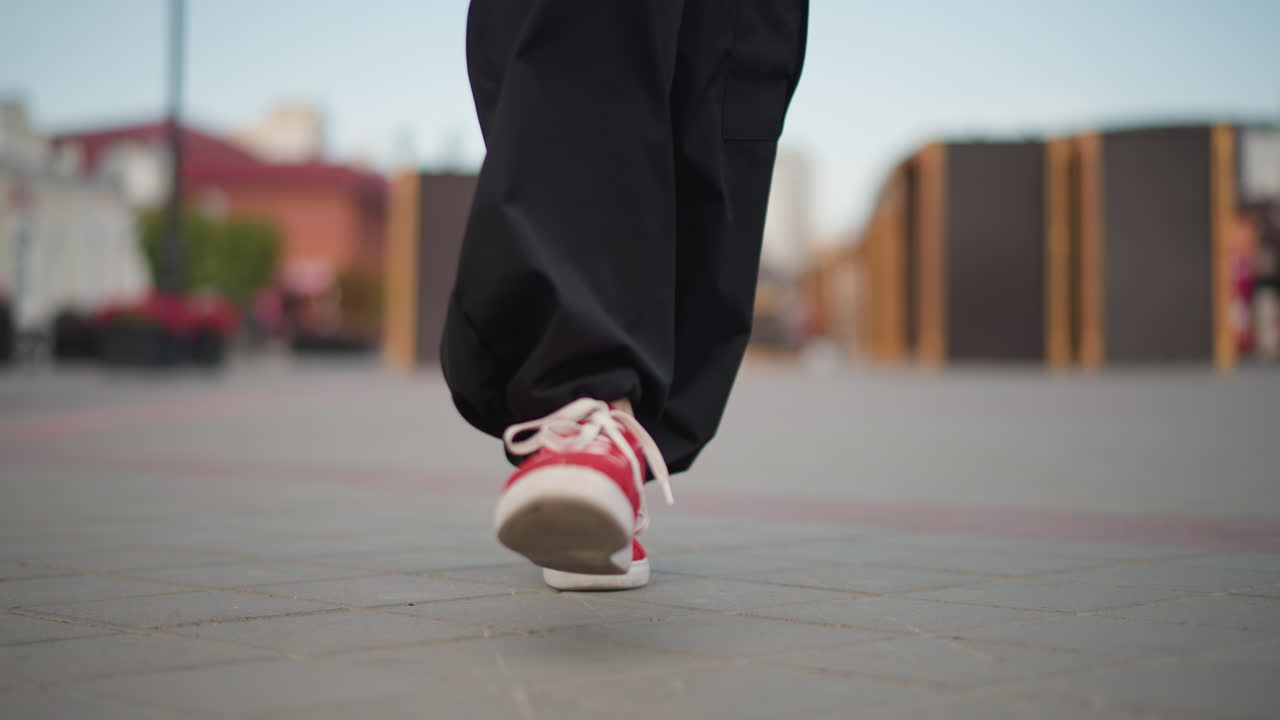 Kırmızı spor ayakkabıların dans ettiği sokak yakın çekimi, bol siyah pantolon, şehir kaldırımlarında hızlı ayak hareketleri, akşam şehir fonu, sığ alan derinliği, enerjik hip hop ritmi, pratik yapan sokak sanatçısı