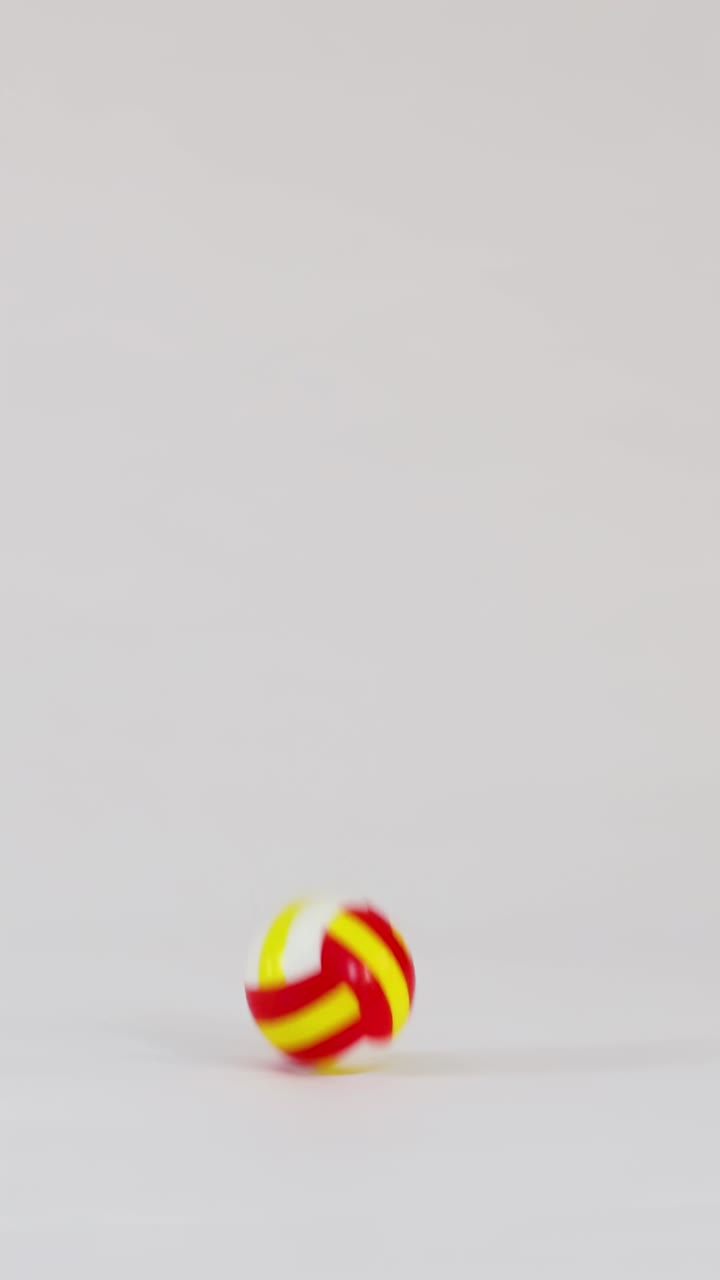 Miniature colorful volleyballs bounce and fly across a clean white studio background in slow motion