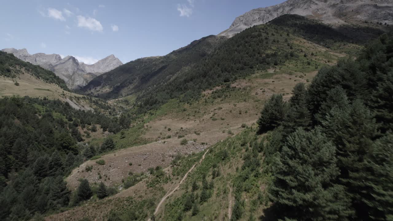 4K low-altitude drone shot over the Western Valleys Natural Park in the Aragonese Pyrenees, Spain. A cinematic aerial view of the prairie leading to Ibón de Acherito with mountains in the background.
