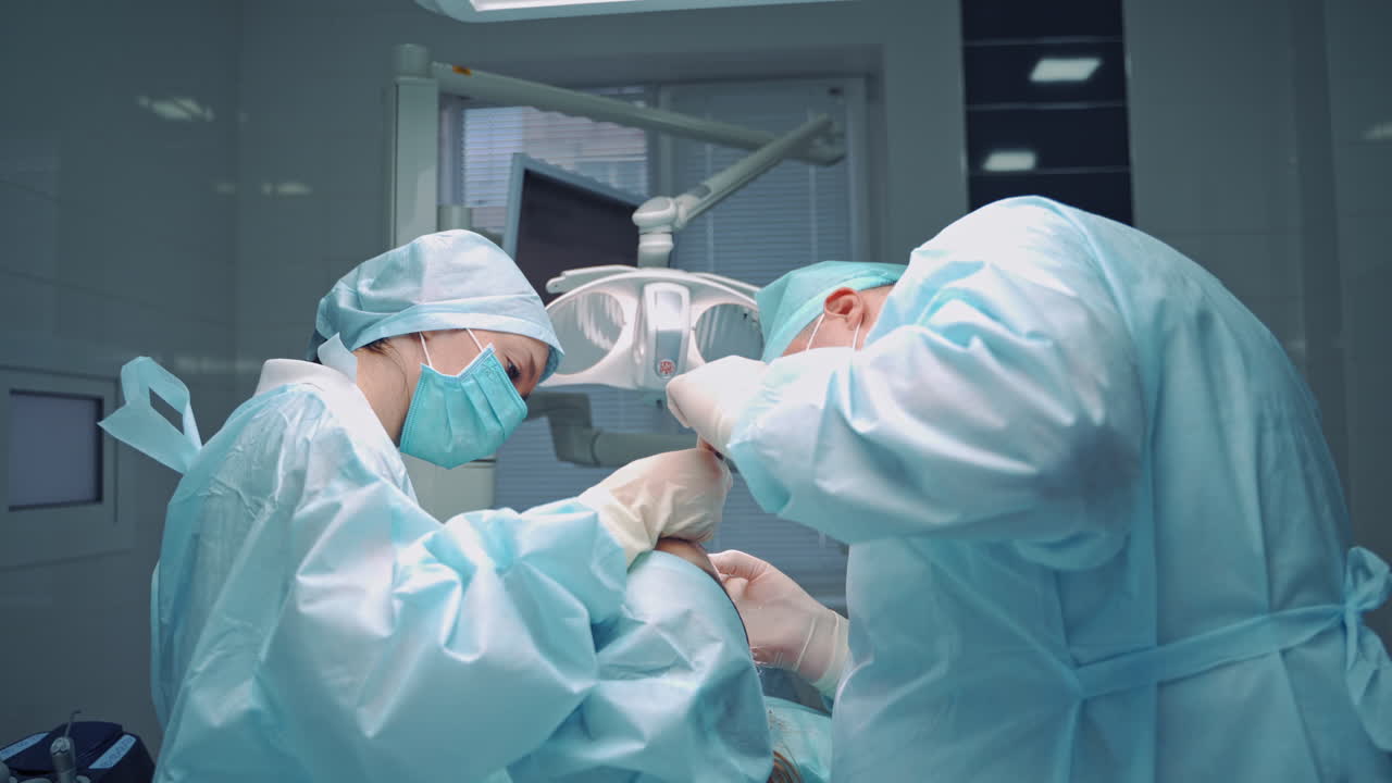 Dentist man and his assistant woman treat patient's teeth on the background of medical center. Oral treatment in clinic by orthodontist and a nurse. Side view.