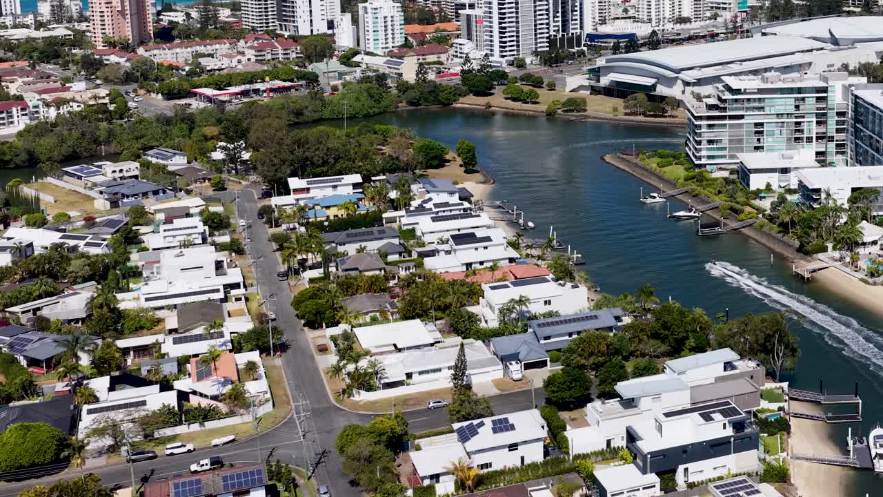 Drone glides above river, residential homes, and modern buildings in bright daylight, Gold Coast