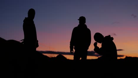 Three-young-motocross-riders-having-a-chat,-smoking-cigarettes-and-enjoying-the-view-of-the-epic-shilouetted-mountainscape