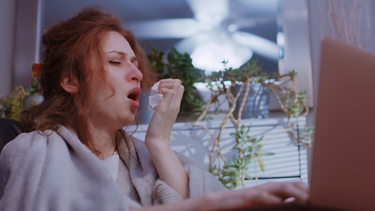백인 여성이 집에서 노트북으로 일하고, 기침하고, 비참합니다.