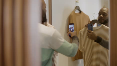 un chico negro feliz tomando una selfie en el camerino sosteniendo una percha.