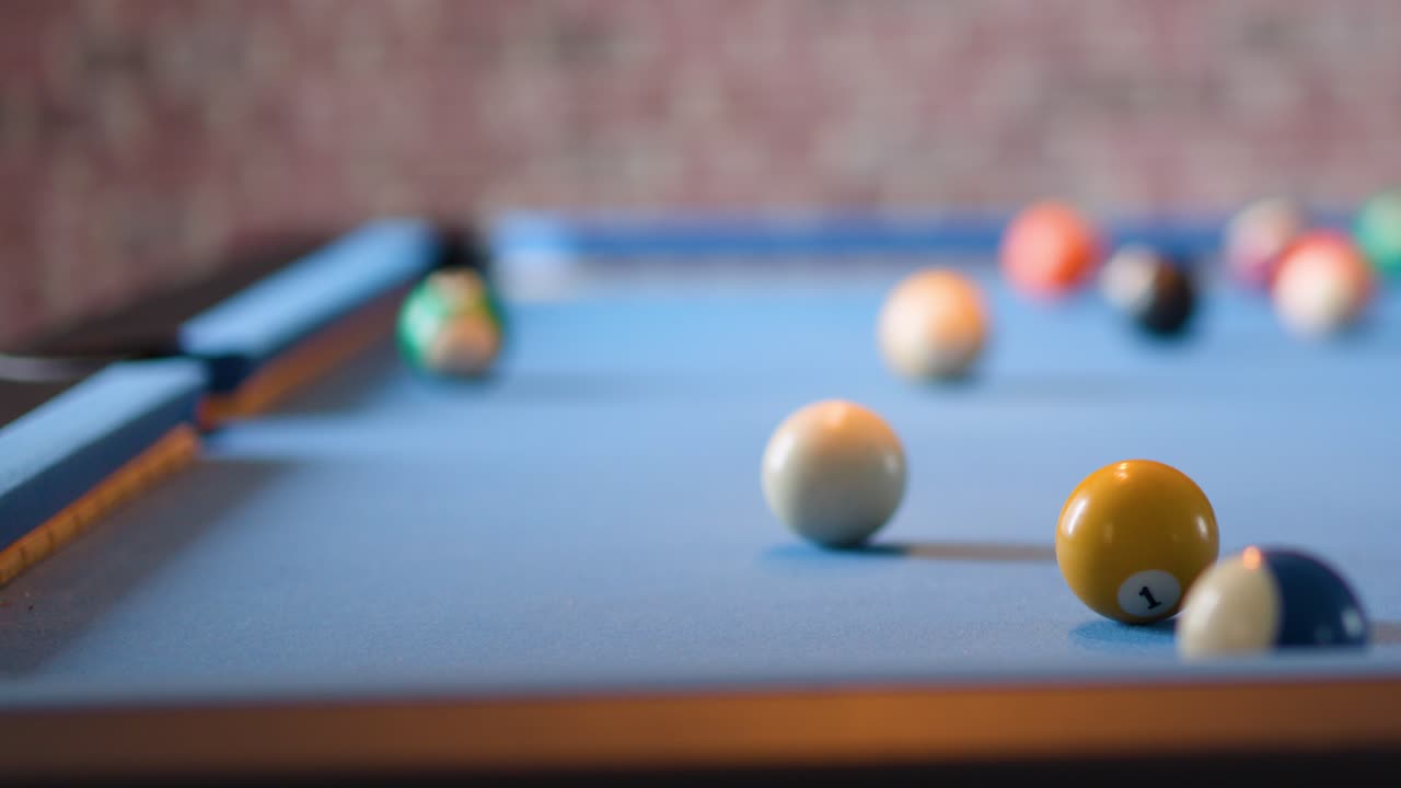 Person hits cue ball on blue pool table, shallow depth of field, soft indoor lighting