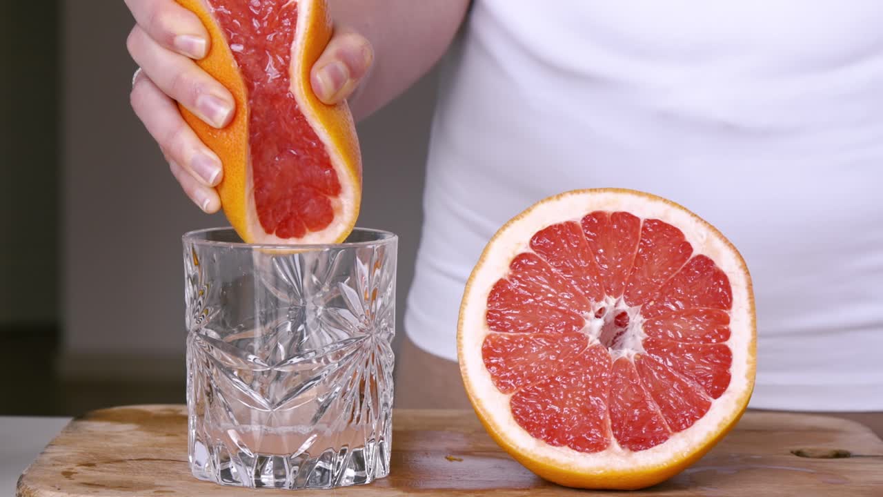 A woman squeezes juice from the grapefruit into a glass on a wooden board. Slow motion