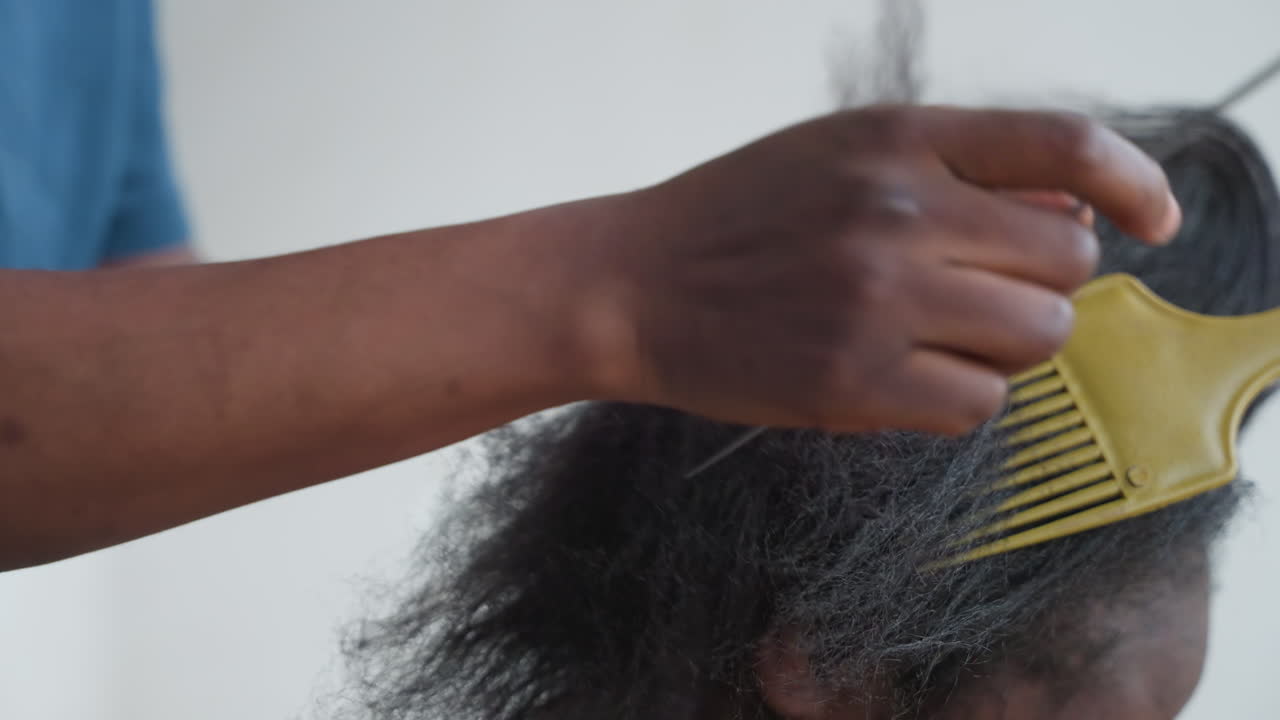 Enges Entwirren der Haare mit gelbem Pick und Stielkamm-Scheitelung, Stylist führt präzises Abteilen und zügiges Kämmen in aktiver Salonsitzung durch, sichtbare Staub- und Frizz-Freisetzung, geschickte Technik, Unterarmbewegung.