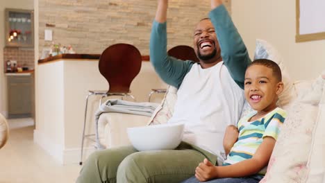 Vater-Und-Sohn-Jubeln-Beim-Fernsehen-Im-Wohnzimmer-4k