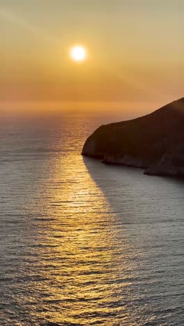 a beautiful view of the sun as it sets over the water with the reflection in the waves overlooking a cliff.