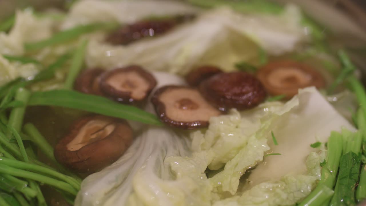 Close-up of shiitake mushrooms added to simmering hotpot with napa cabbage and greens