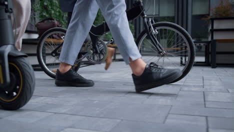 closeup managers legs walking with bicycle electric scooter at downtown area.