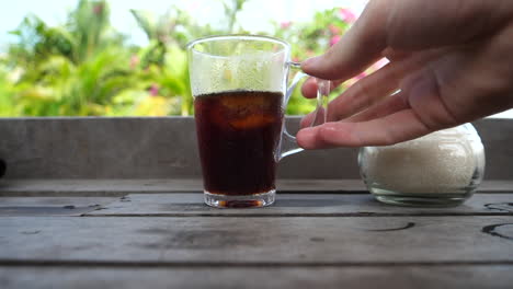 Hand-grabbing-an-iced-beverage-to-take-a-drink-with-a-tropical-background