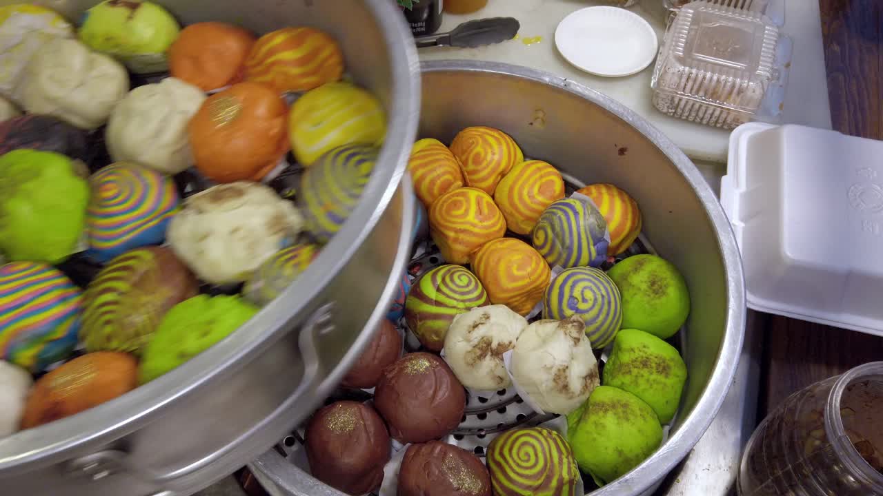 Bao colorés cuits à la vapeur dans une marmite avec des pinces pour une présentation culinaire éclatante
