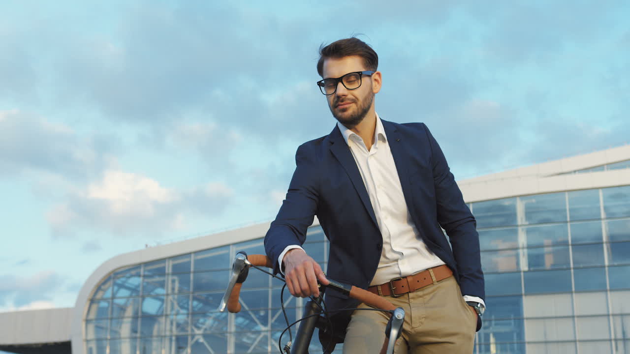 자전거에 기대어 거대한 건물에 가까운 카메라를 보면서 웃고 있는 잘생긴 사업가