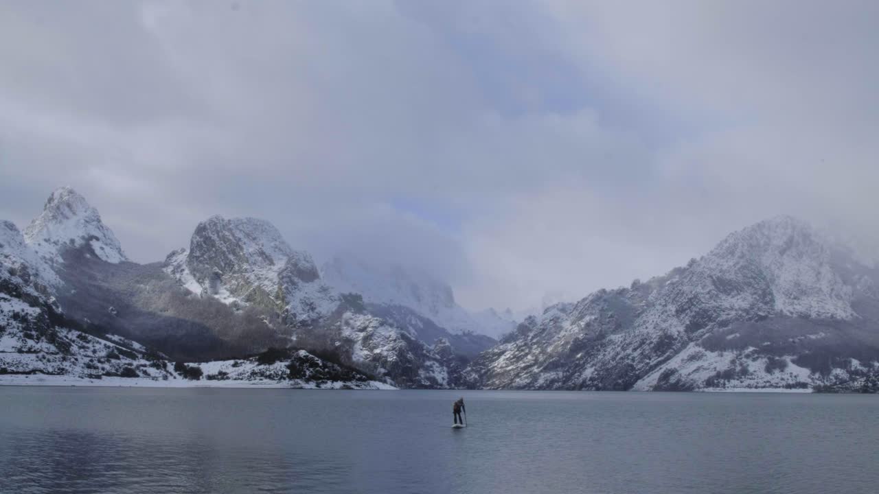 hombre en paddle board entre el agua y las montañas en la costa