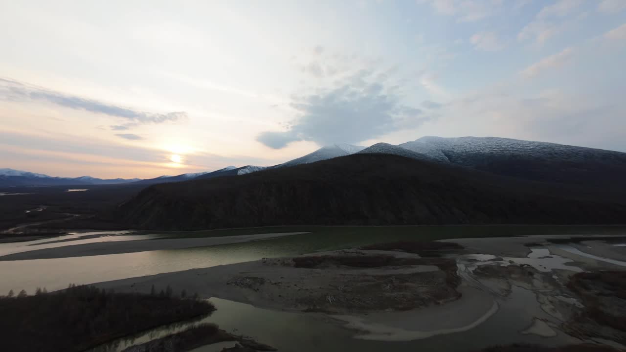 A mesmerizing exploration of untouched wilderness at sunset, highlighting the peaceful flow of the river against majestic mountains. The warm sunlight casts a golden hue over the landscape.