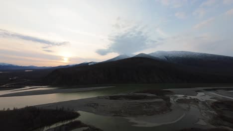 a mesmerizing exploration of untouched wilderness at sunset, highlighting the peaceful flow of the river against majestic mountains. the warm sunlight casts a golden hue over the landscape.