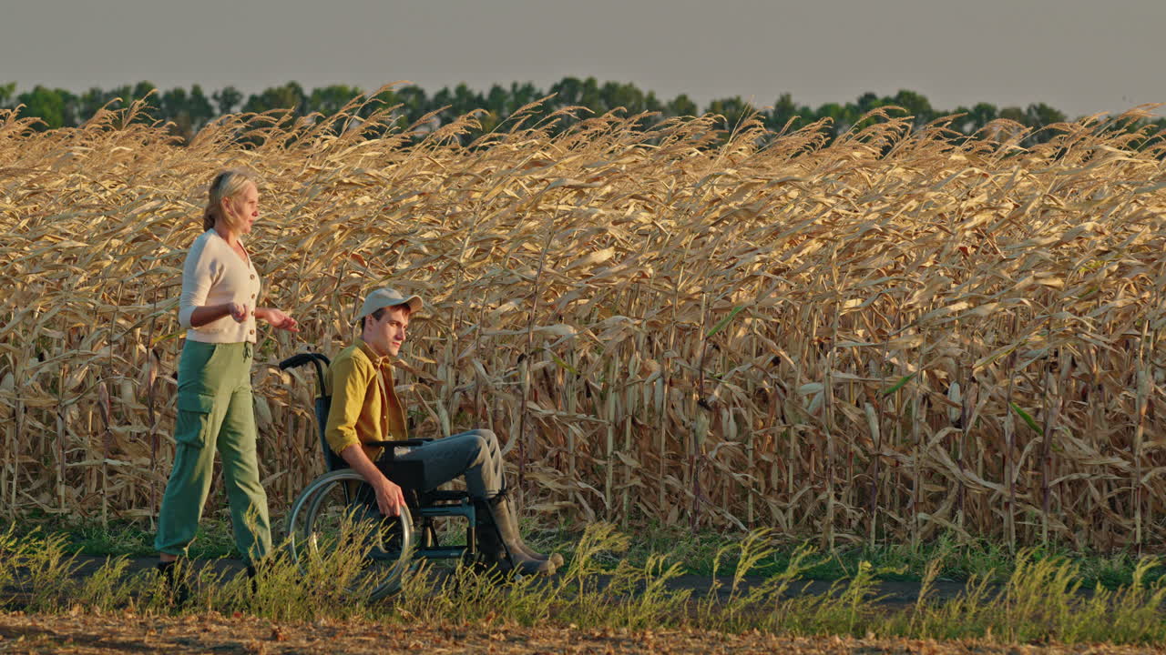 해가 지는 동안 옥수수  을 가로질러 체어 에 앉아 있는 남자 를 돕는 여자