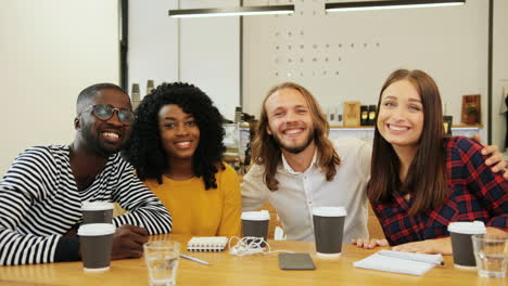 multiethnic group of friends smiling and looking at camera sitting at a table in a cafe