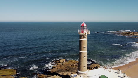 disparo aéreo hacia atrás que revela un faro en las rocas y la costa