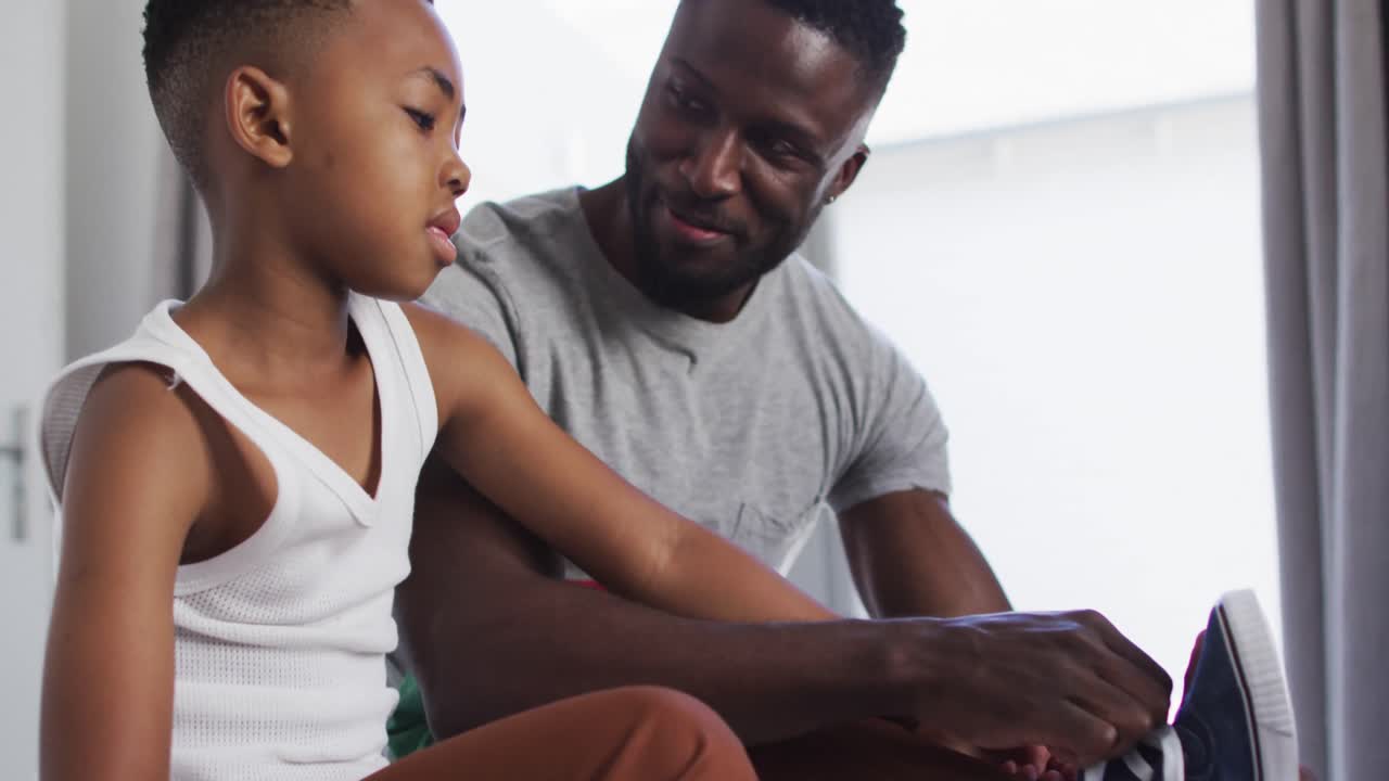 African american father helping his son with getting dressed in bedroom