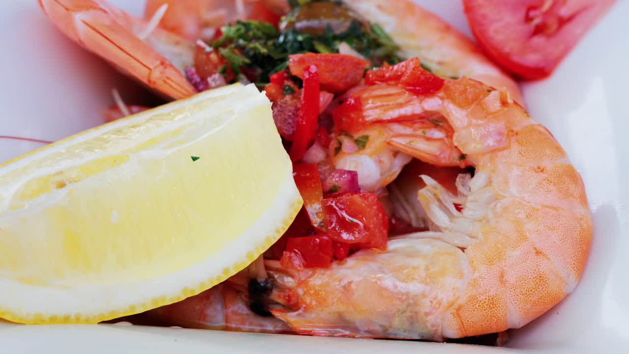 Close up of cooked shrimp with a slice of lemon and herbs on a white plate at a restaurant