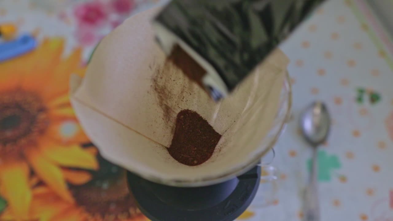 Pouring dark aromatic coffe into a brown paper coffe filter sitting in a dripper. Preparation for brewing a coffe using an alternative method. Home made brew with a dripper.