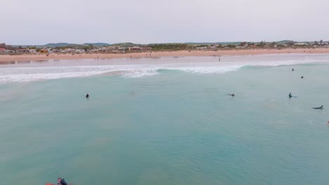 dolly aéreo a la playa desde el océano abierto mientras los surfistas atrapan olas en españa