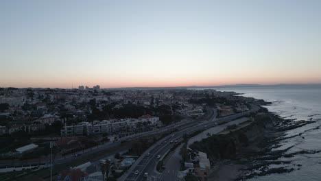 Aerial-video-of-coastal-residential-area-during-sunset-time,-road-with-car-traffic-along-the-shore-highway,,-coastal-life-concept