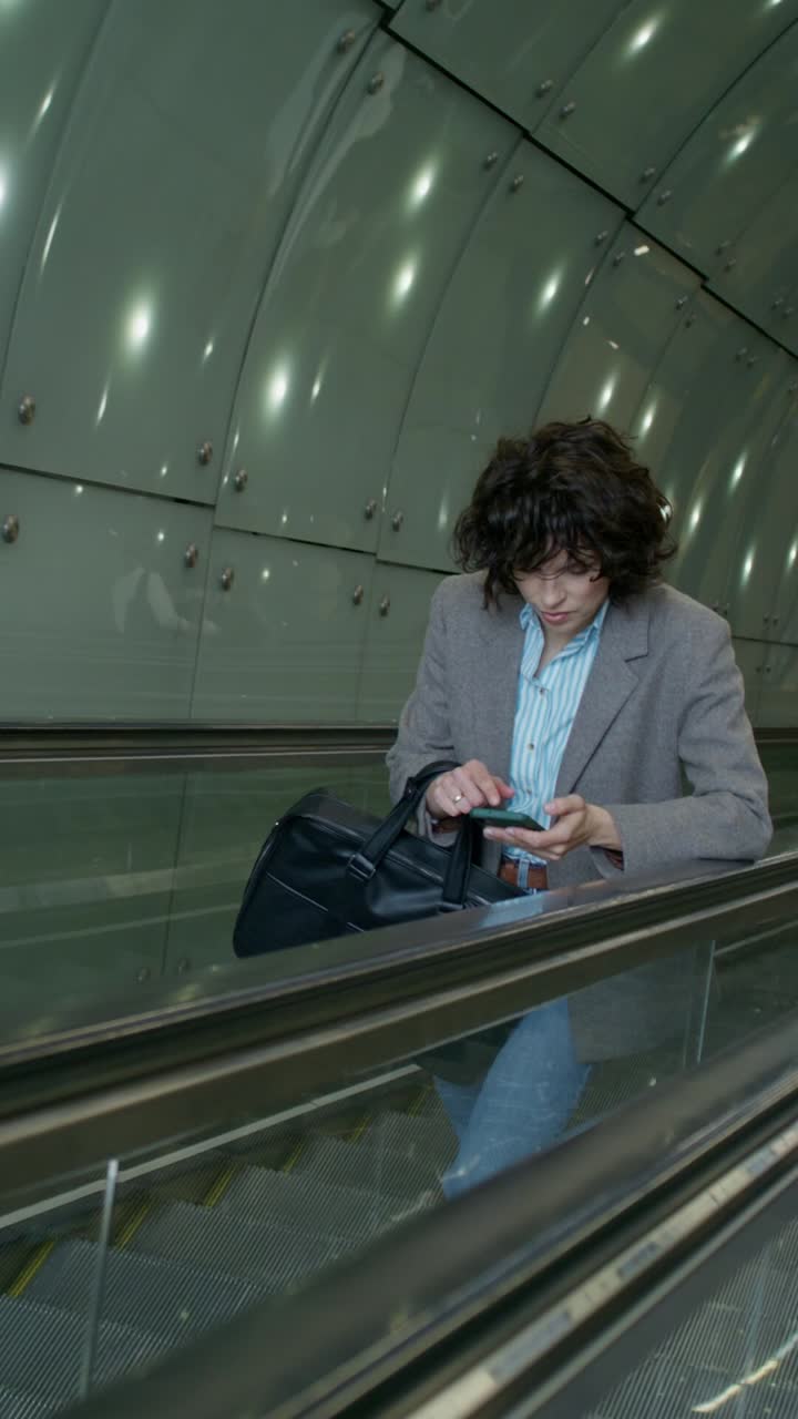 mujer usando el teléfono en una escalera mecánica en un túnel moderno